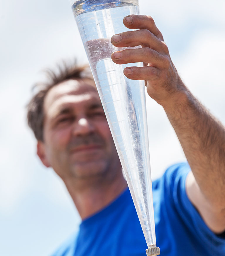 Mitarbeiter von BauGrund Süd hält Wasserprobe in einem Messzylinder vor blauem Himmel